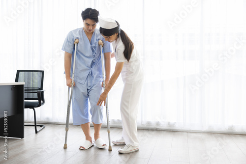 Female nurse or physician helping young male patient knee pain standing walking with clutch  Osteoarthritis Physical therapy