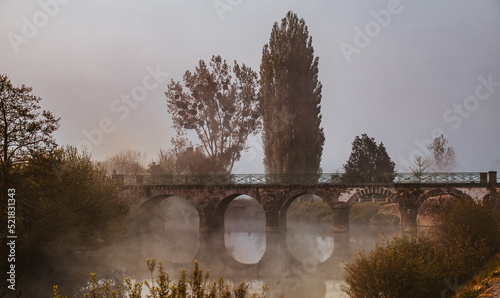 An old stone bridge in the fog over a river in Normandy, France