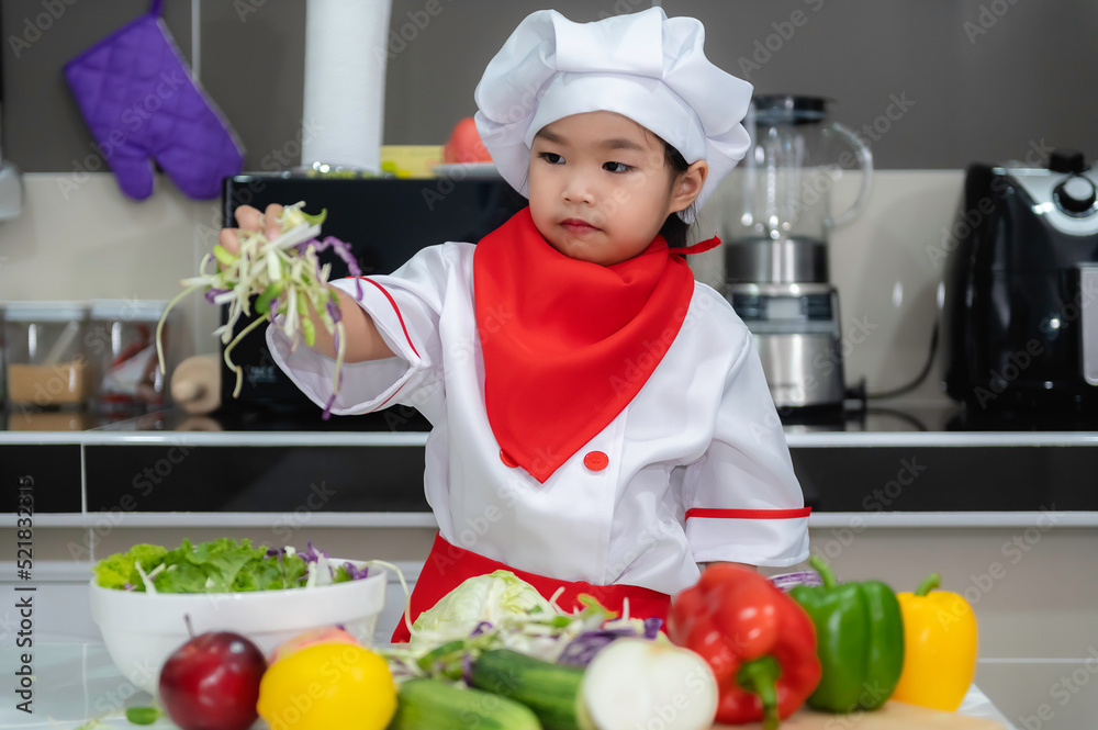 Cute asian girl wear chef uniform with a lot of vegatable on the table in the kitchen room,Make food for eat dinner,Funny time for kids Cute asian girl wear chef uniform with a lot of vegatable on the table in the kitchen room,Make food for eat dinner,Funny time for kids