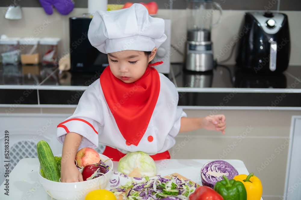 Cute asian girl wear chef uniform with a lot of vegatable on the table in the kitchen room,Make food for eat dinner,Funny time for kids Cute asian girl wear chef uniform with a lot of vegatable on the table in the kitchen room,Make food for eat dinner,Funny time for kids