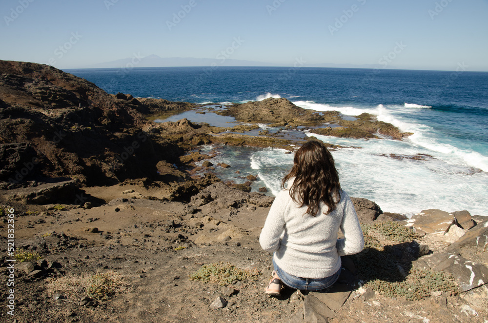 Woman and coastal landscape with the island of Tenerife to the background. Galdar. Gran Canaria. Canary Islands. Spain.
