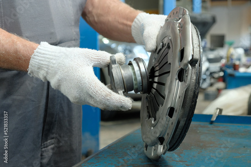 An auto mechanic holds a clutch kit. Compliance and integrity control of the drive disc, the driven disc and the exhaust bearing. Repair and maintenance in a car service center.