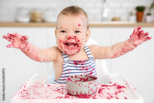 Happy baby in high chair with messy face and hands photo