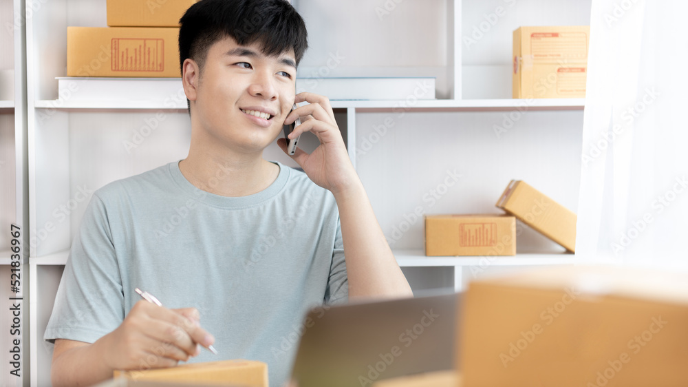 Man selling products online was talking on the phone or chat to receive an order from a customer and list in a notebook, Online shopping SME entrepreneur, Packing box, Sell online, Freelance working. Man selling products online was talking on the phone or chat to receive an order from a customer and list in a notebook, Online shopping SME entrepreneur, Packing box, Sell online, Freelance working.
