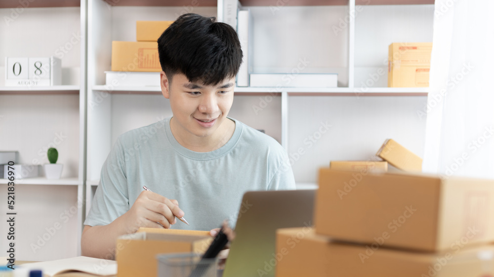 Young Asian man is writing down the customer's details and addresses on the notebook or box in order to prepare for shipping according to the information, Packing box, Sell online, freelance working. Young Asian man is writing down the customer's details and addresses on the notebook or box in order to prepare for shipping according to the information, Packing box, Sell online, freelance working.
