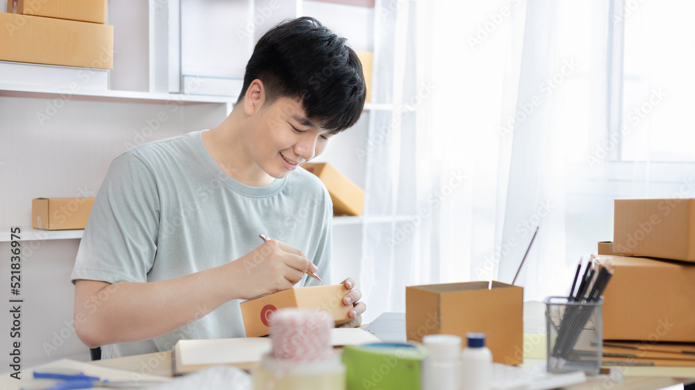 Young Asian man is writing down the customer's details and addresses on the notebook or box in order to prepare for shipping according to the information, Packing box, Sell online, freelance working. Young Asian man is writing down the customer's details and addresses on the notebook or box in order to prepare for shipping according to the information, Packing box, Sell online, freelance working.