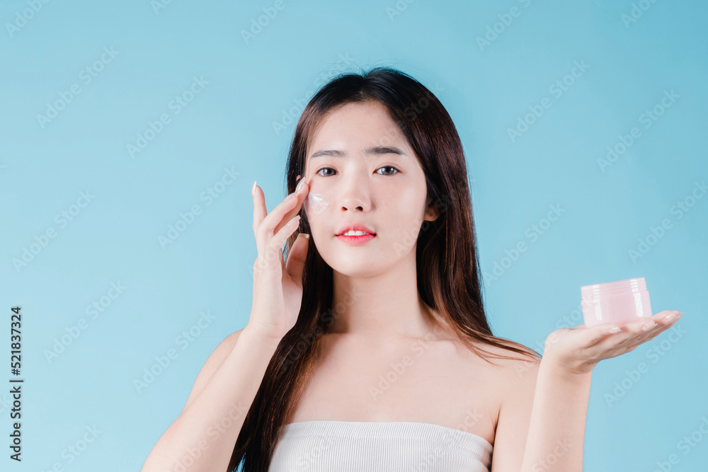 Asian beauty woman applying moisturizer, lotion, serum on facial by skin care on the blue background