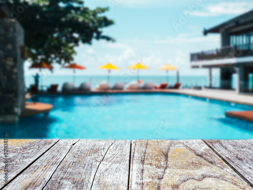 Close-up empty space on old wooden plank table or deck floor in front of the blurred pool  beach and open sky background on sunny day. Empty space for product at poolside  summer background.
