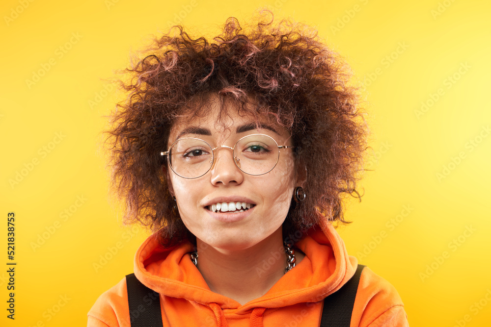 Positive kazakh student girl with afro hairstyle and backpack smiling on yellow studio background Positive kazakh student girl with afro hairstyle and backpack smiling on yellow studio background