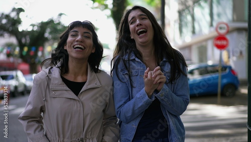 Female friends laughing and smiling while while walking in city sidewalk. Authentic real expression laugh and smile © Marco