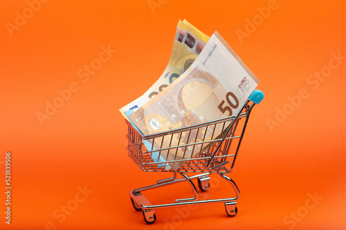 Euro banknotes of different nominals in the shopping cart on bright orange background photo