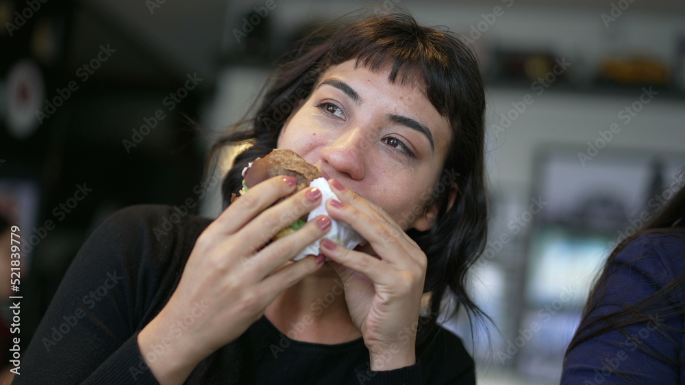 One hispanic woman eating burger. A latin american girl eats fast food cheeseburger One hispanic woman eating burger. A latin american girl eats fast food cheeseburger