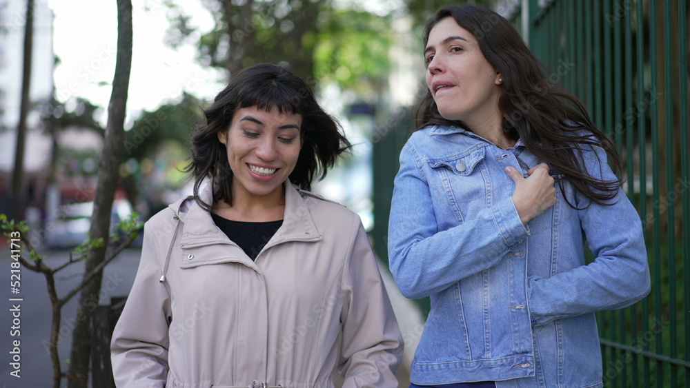 Two women in conversation walking in city street. Female friends talking Two women in conversation walking in city street. Female friends talking