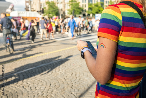 Female with rainbow LGBT flag tatoo on her arm on a street of Amsterdam during Netherlands Pride month celebrations. City with people on background. Symbol of social movement for diversity.