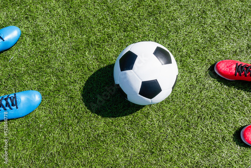 Soccer football background. Soccer ball and two pair of football sports shoes on artificial turf soccer field with shadow from football goal net on sunny day outdoors. Top view