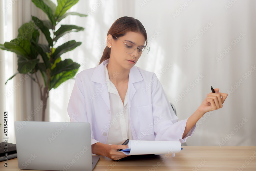 Young woman doctor using laptop computer and looking document paper about patient for diagnostic at clinic, physician female working and reading document on clipboard, one person, medical concept.