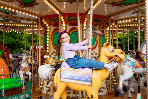 a child girl in an amusement park rides on a carousel and smiles with happiness, the concept of weekends and school holidays © Any Grant