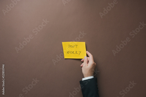 Businessman placing yellow paper with Dont worry sign over brown background photo