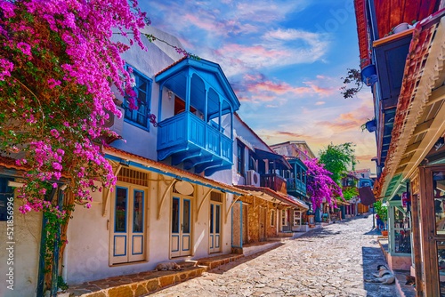 Fototapeta Naklejka Na Ścianę i Meble -  Old colored street view. White houses with wooden blue balconies and pink flowers in Kas city, Turkey