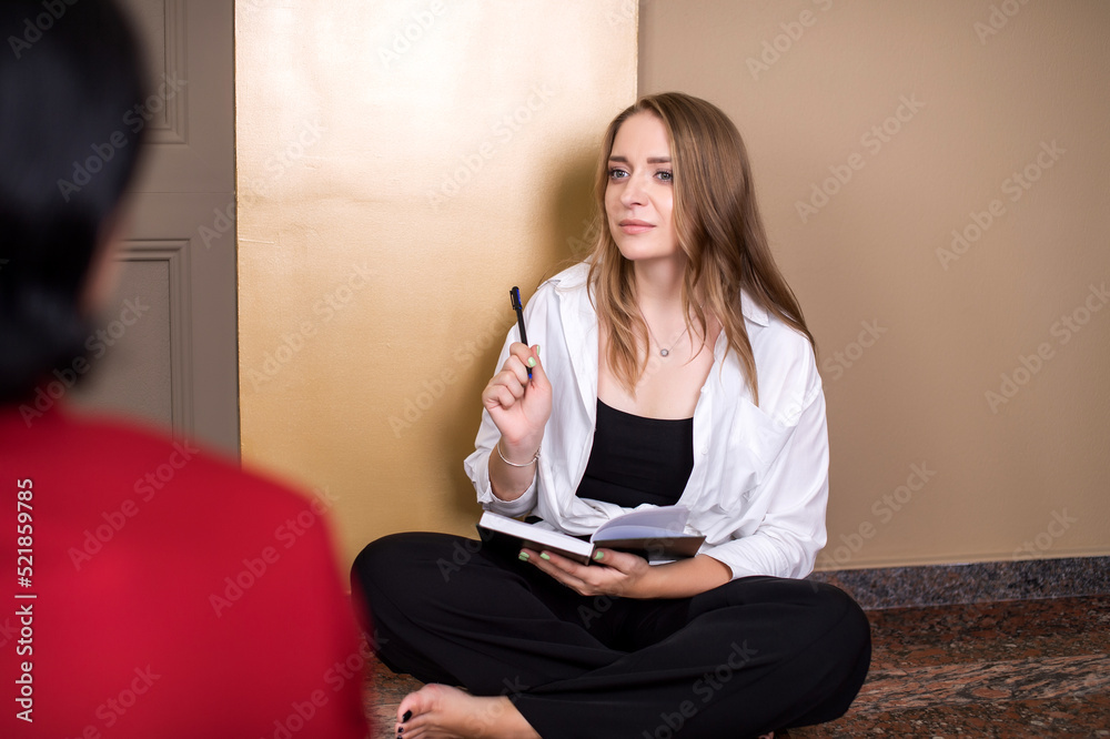 A cute girl sitting on the floor raised her pen up near the notebook for writing A cute girl sitting on the floor raised her pen up near the notebook for writing