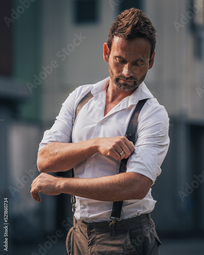Attractive man in urban scenery is rolling up his shirts sleeve