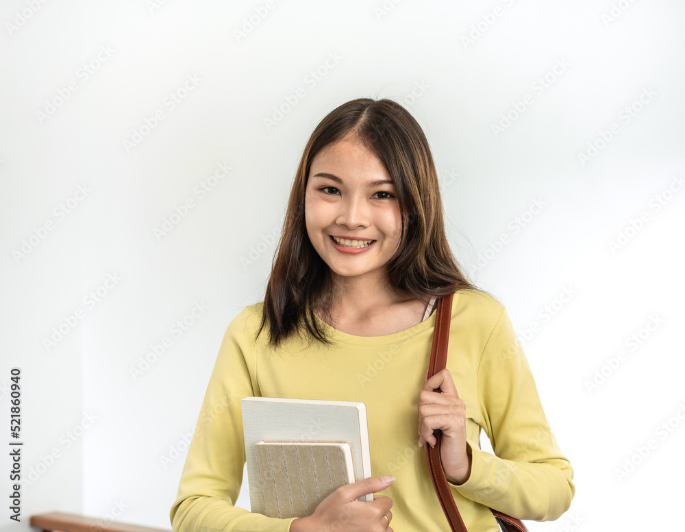 Young woman student is standing and smiling to looking on camera while holding books and bags Young woman student is standing and smiling to looking on camera while holding books and bags