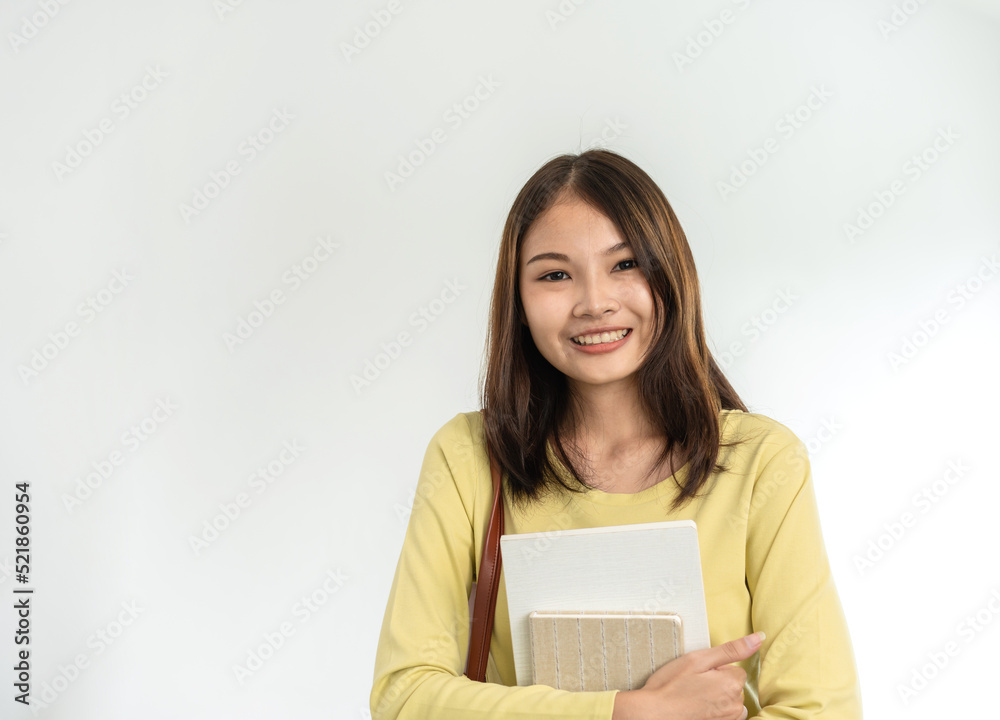 Young woman student is standing and smiling to looking on camera while holding books and bags Young woman student is standing and smiling to looking on camera while holding books and bags
