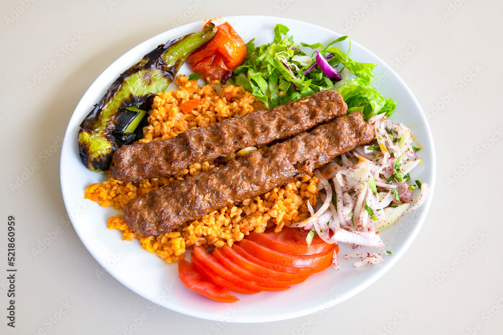 Grilled Turkish Adana, Urfa  Kebab with grilled vegetables, onion and rice on plate. Adana durum .