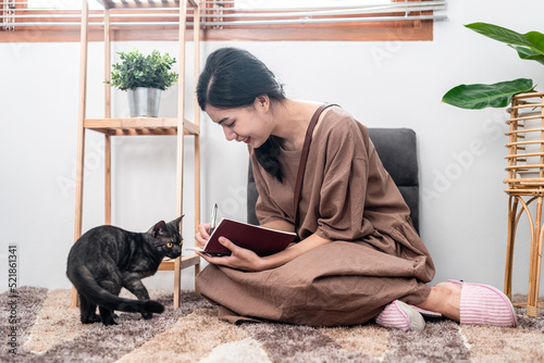 Beautiful woman is writing notes on notebook and playing with a lovely cat while sitting to relaxation © Katcha