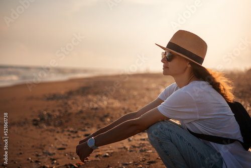 Obraz na płótnie Young happy relaxed woman in a hat sitting on the seashore at sunset w salonie
