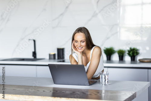 Happy young woman in the kitchen reading he news on her laptop