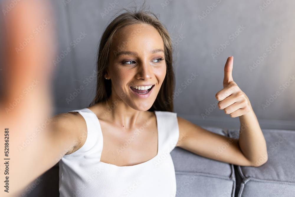 Cheerful woman showing thumb up while using mobile phone on sofa at home Cheerful woman showing thumb up while using mobile phone on sofa at home