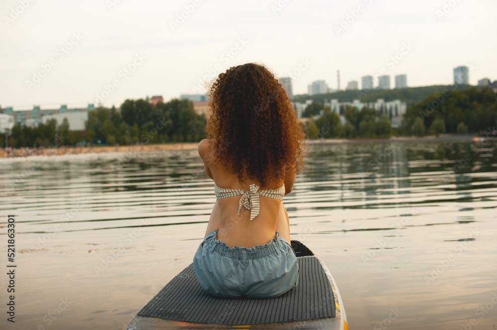 A white girl with afro pigtails is resting in seclusion. Girl swims on a SUP board
