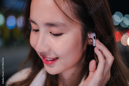 Asian businesswoman use wireless earbuds listening music in the modern city at night