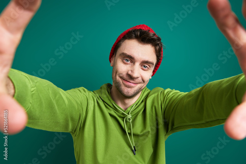 Handsome young man looking through a finger frame while standing against green background