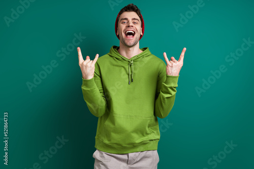 Handsome young man gesturing and smiling while standing against green background