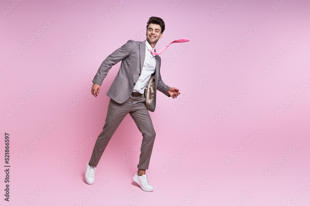 Excited young man in full suit smiling while moving against pink background Excited young man in full suit smiling while moving against pink background