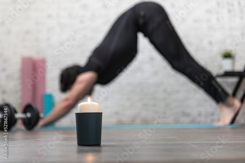 Fototapeta Naklejka Na Ścianę i Meble -  Close-up of candle with training man on background. Yoga poses and stretching concept	
