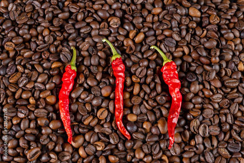 Three red hot chili peppers on a background of roasted coffee beans. The concept of coffee with spices in a modern kitchen.