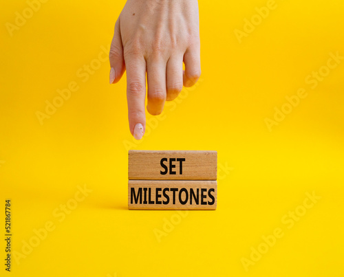 Set milestones symbol. Concept word Set milestones on wooden blocks. Beautiful yellow background. Businessman hand. Business and Set milestones concept. Copy space