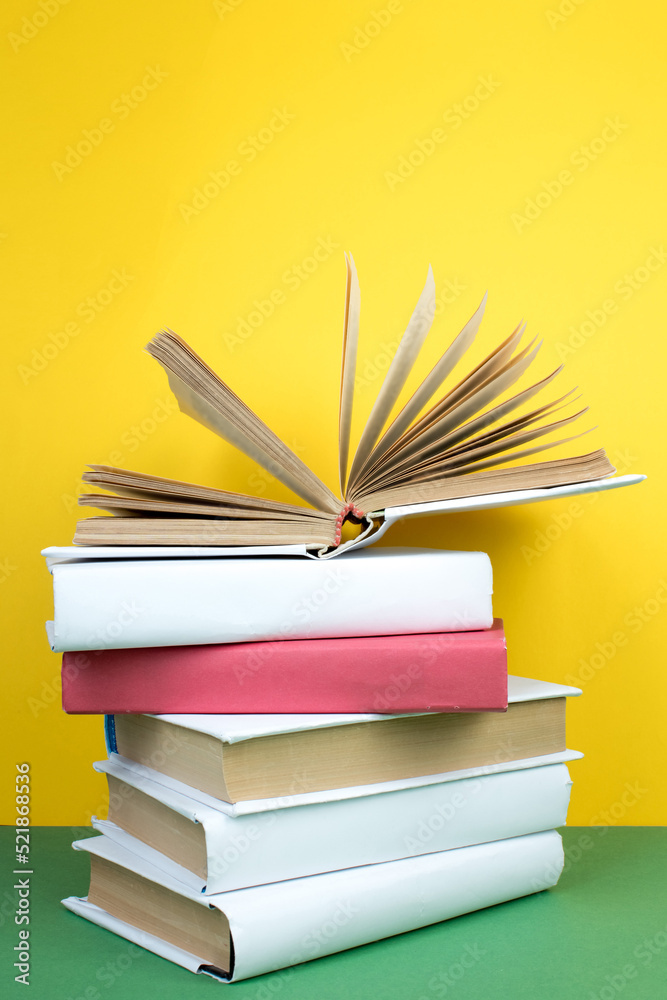 Fototapeta premium Book stacking. Open hardback books on wooden table and green background. Back to school. Copy space for ad text.