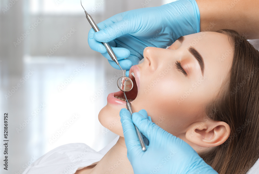 Fototapeta premium A dentist doctor treats caries on a tooth of a young beautiful woman in a dental clinic. Tooth filling.