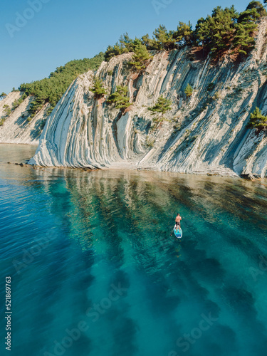 Man on stand up paddle board in blue sea. Surfer walking on SUP board in sea with incredible landscape. Aerial view