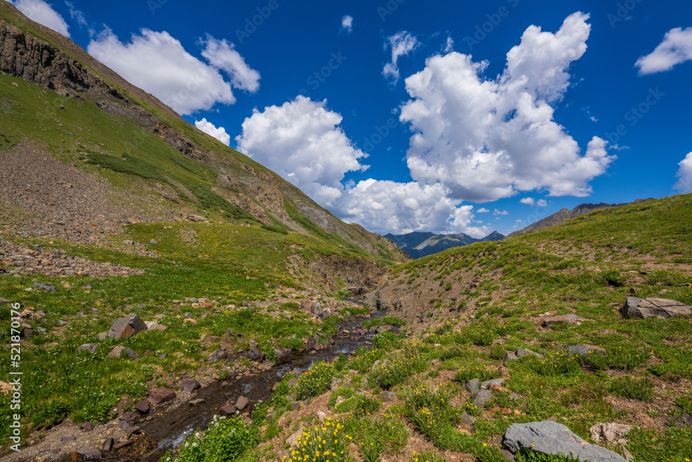 alpine stream in tundra canyon with big clouds and blue sky