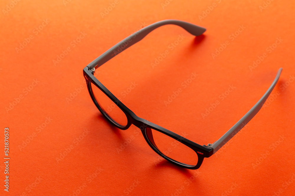 Stylish eyeglasses over orange background. Glasses selection, eye test, vision examination at optician, fashion accessories concept. Top view, flat lay. Stylish eyeglasses over orange background. Glasses selection, eye test, vision examination at optician, fashion accessories concept. Top view, flat lay.