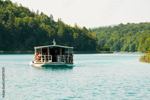Quadro em tela Boat with group of tourists sails on deep turquoise lake surrounded by green forestry hills