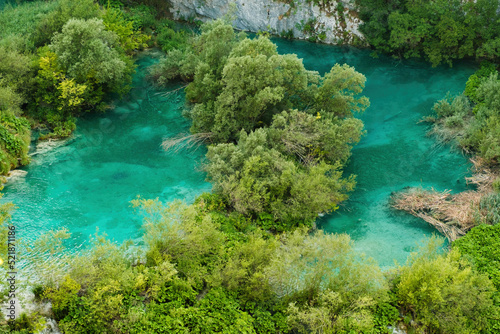 Small green islands among turquoise-colored transparent water of lake surrounded by mountains. Breathtaking landscape of natural reserve on Plitvice lakes upper view