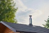 Stainless steel metal chimney pipe on the roof of the house against the sky.