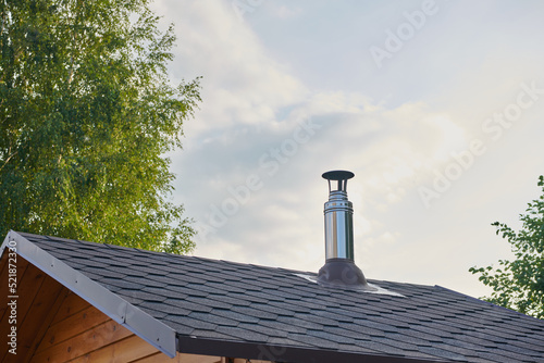 Foto Stainless steel metal chimney pipe on the roof of the house against the sky