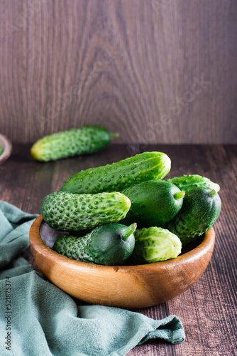 Fresh whole cucumbers in a bowl and on a wooden table. Diet organic food. Vertical view
